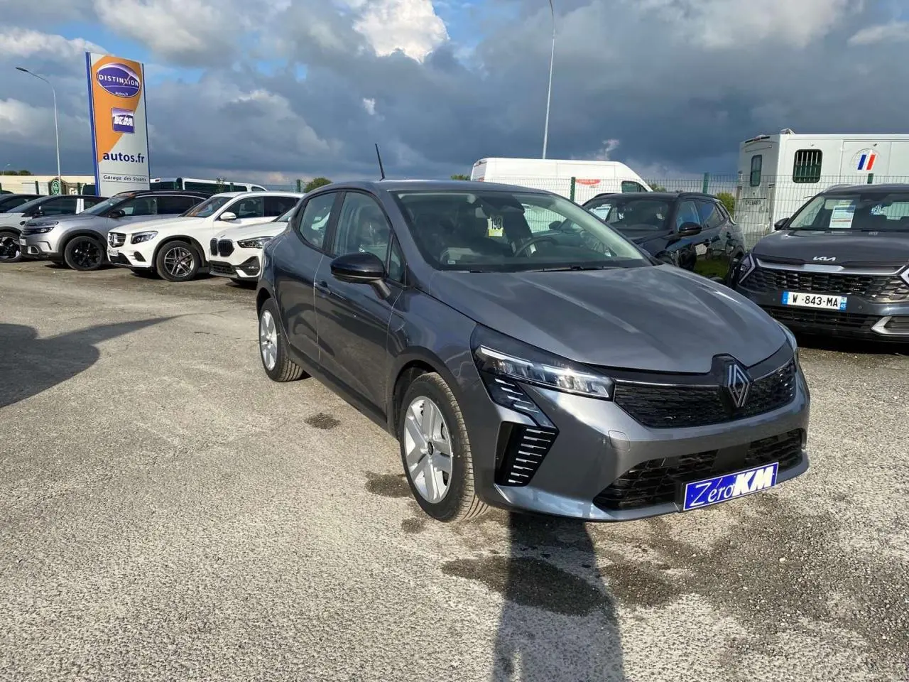 Renault Clio gris schiste vue 3/4 avant droit sur parking, mettant en valeur ses phares LED et sa calandre noire.