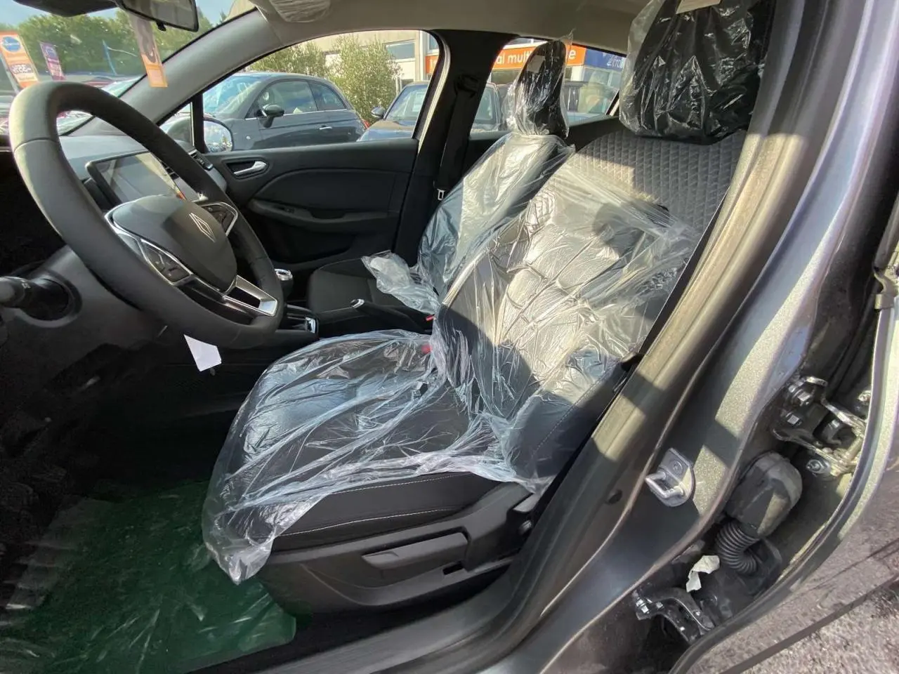 Intérieur côté conducteur d'une Renault Clio 2025 gris schiste, sièges avant protégés par film plastique.