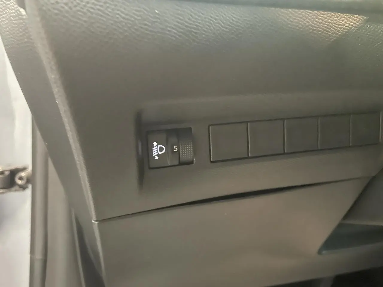 Détail intérieur montrant la molette de réglage des projecteurs sur la console côté conducteur de la Peugeot 208 gris Artense.