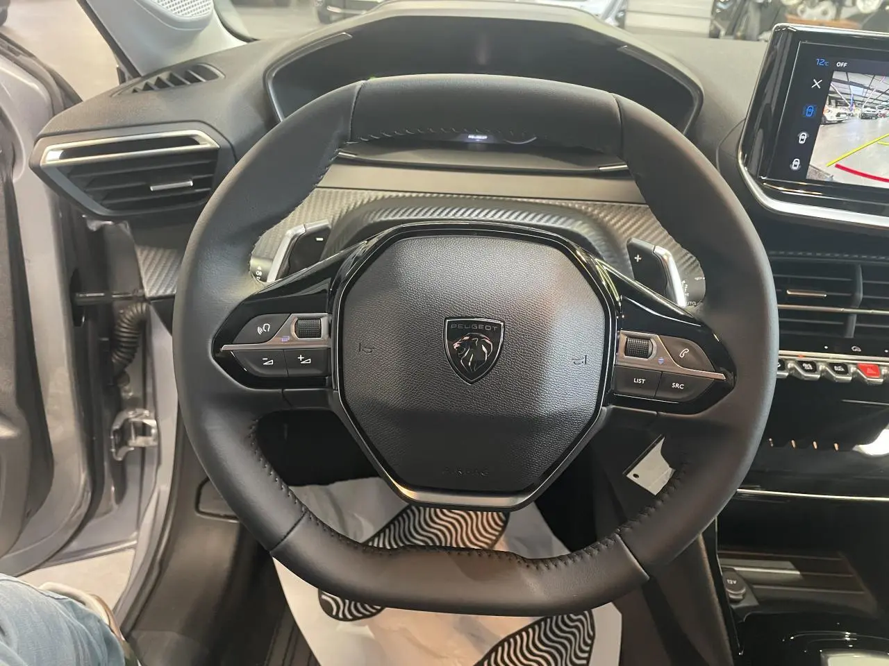 Vue rapprochée du volant cuir noir de la Peugeot 208 2025 avec commandes intégrées et tableau de bord carbone.