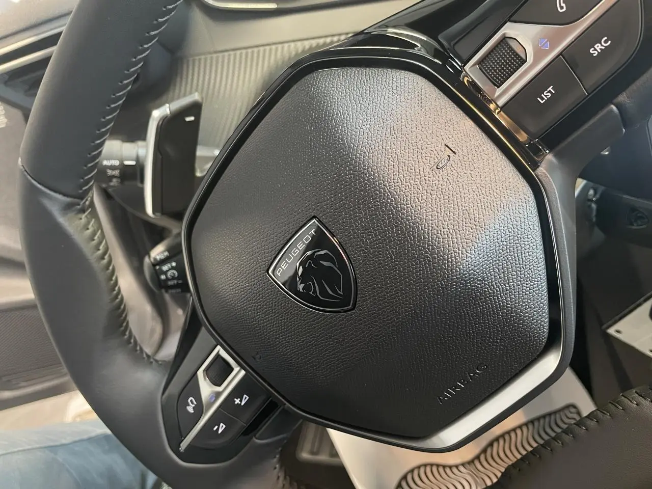 Gros plan sur le volant cuir noir de la Peugeot 208 2025 avec logo lion et commandes intégrées.