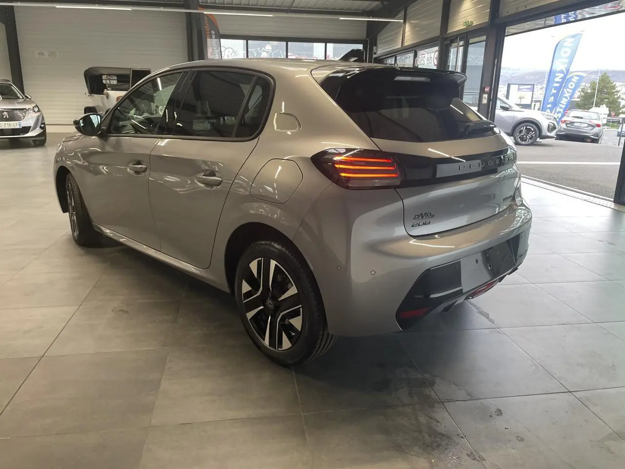 Vue 3/4 arrière droite d'une Peugeot 208 gris Artense avec feux arrière LED et jantes alliage diamantées.