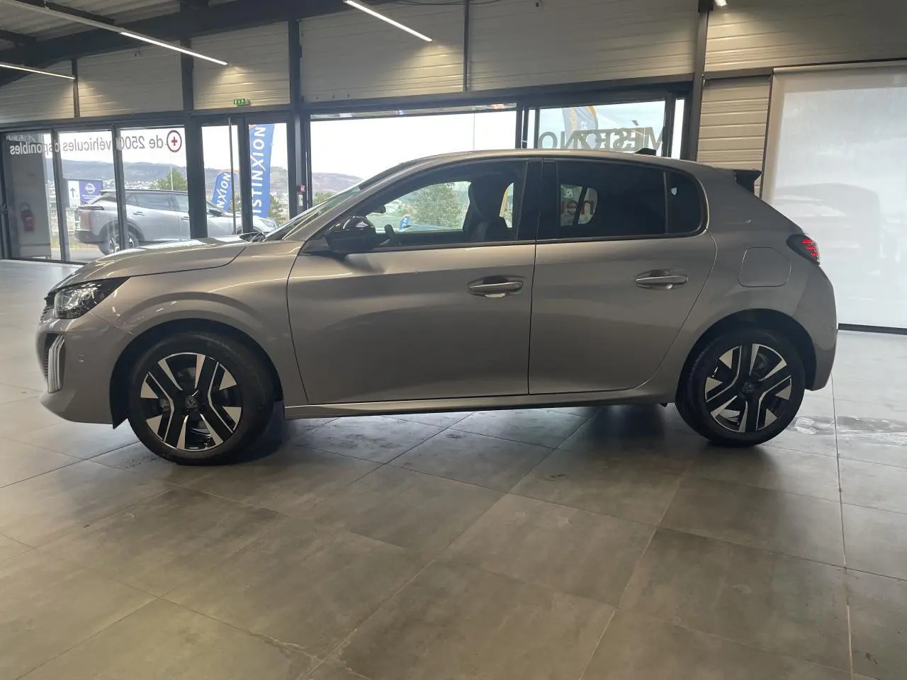 Vue de profil côté gauche d'une Peugeot 208 gris Artense avec jantes alliage 16 pouces en intérieur showroom.