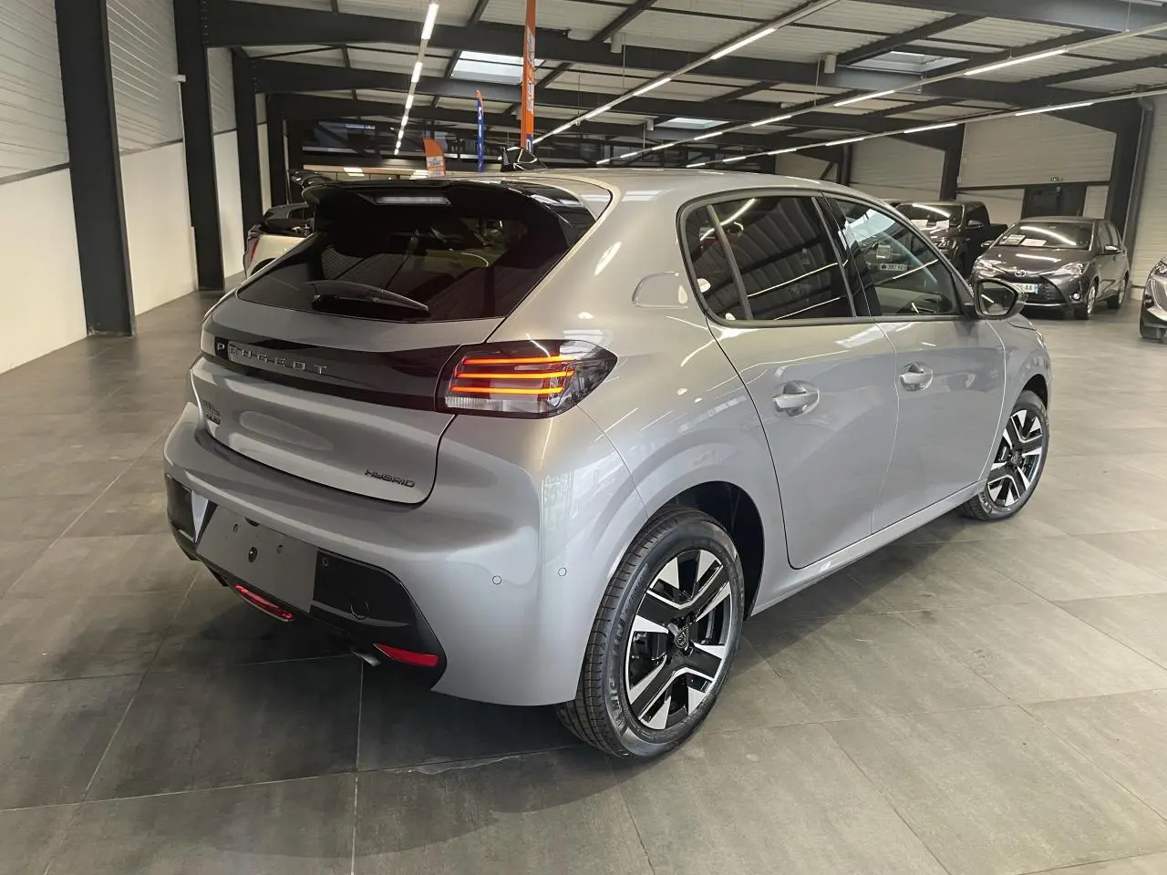 Peugeot 208 gris Artense vue 3/4 arrière droit en intérieur avec feux arrière LED et jantes alliage bi-tons.