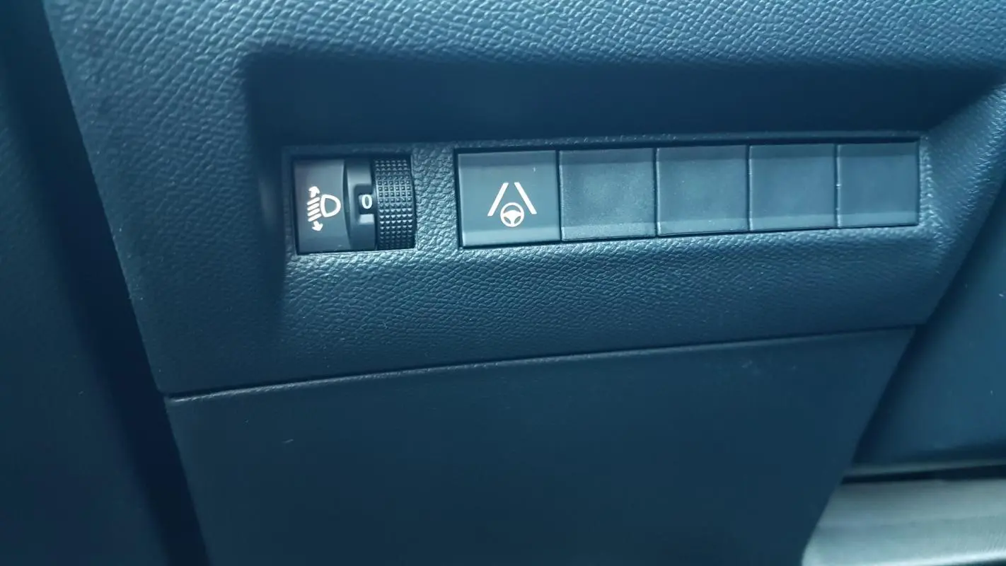 Détail intérieur montrant les commandes de réglage des phares et d’aide au maintien de voie sur Peugeot 2008 noir.