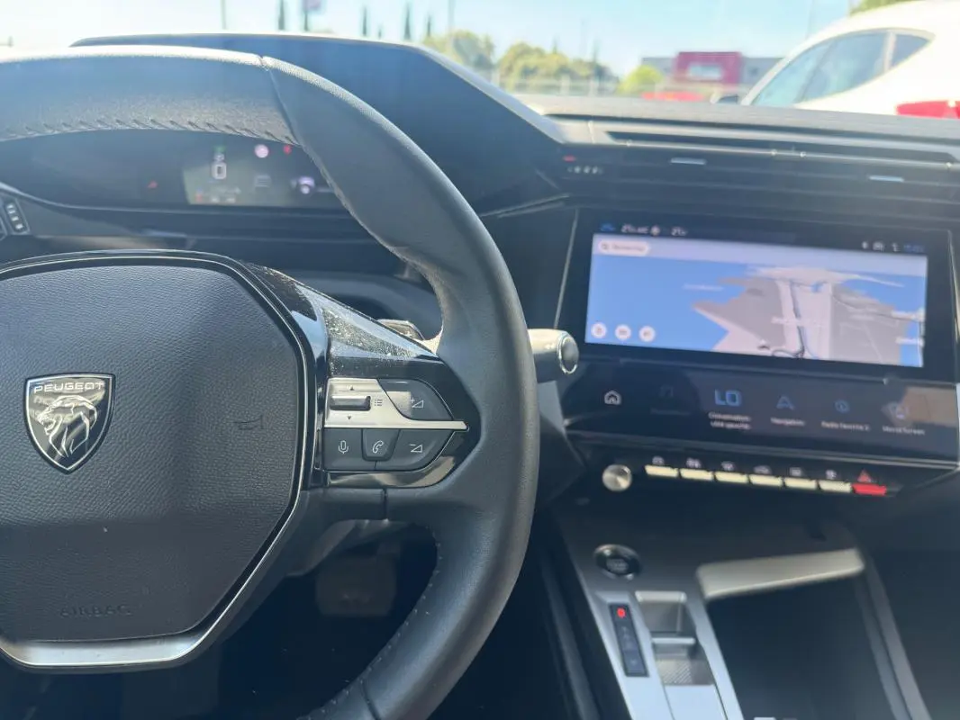 Vue intérieure du tableau de bord et volant de la Peugeot 308 Hybrid gris, avec écran tactile et commandes au volant visibles.