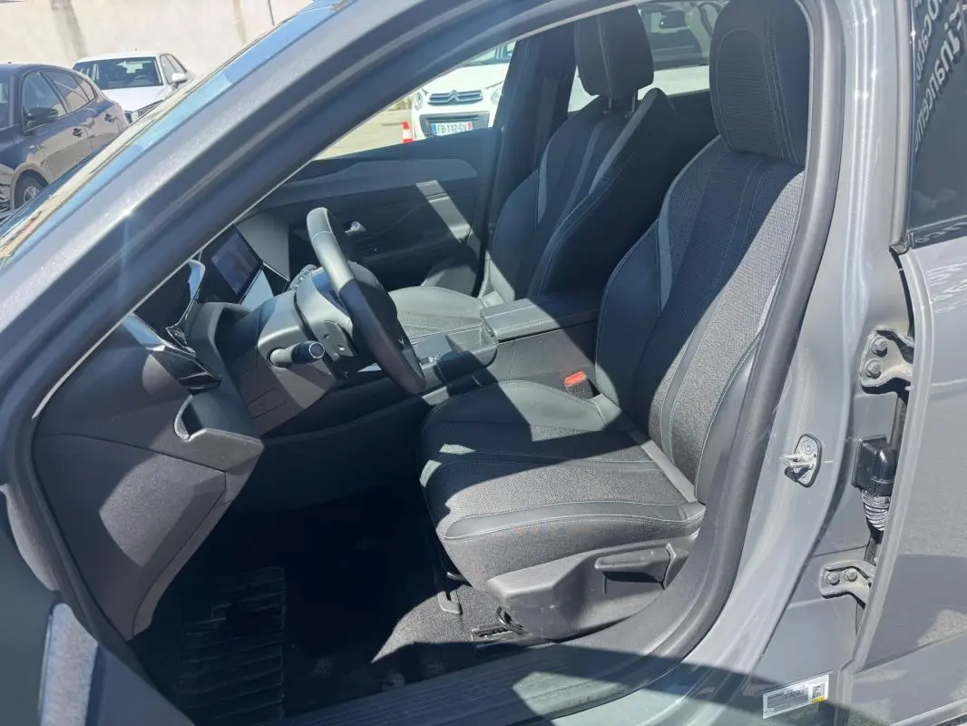 Intérieur avant de la Peugeot 308 Hybrid gris, vue côté conducteur avec sièges en tissu et accoudoir central visible.