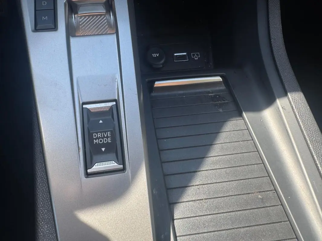 Gros plan sur la console centrale grise de la Peugeot 308 Hybrid 2025 avec bouton Drive Mode et prise USB visible.