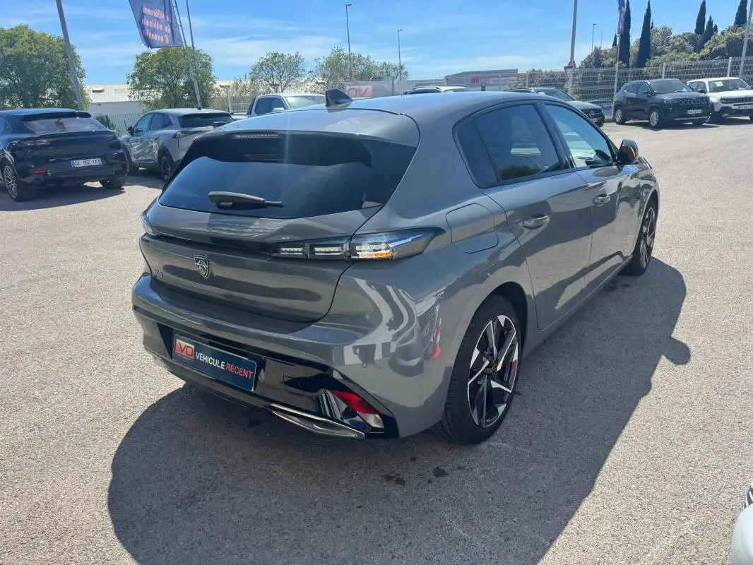 Vue 3/4 arrière droite d'une Peugeot 308 Hybrid gris métallisé avec jantes alliage 17 pouces sur parking extérieur.
