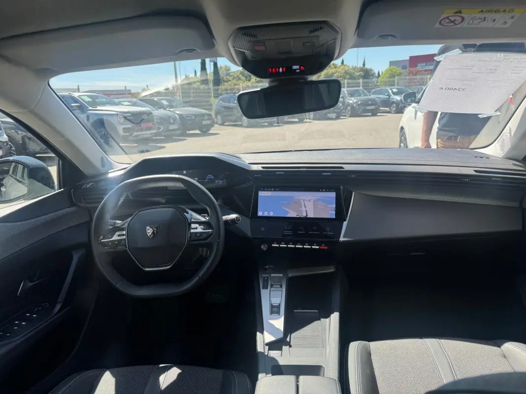 Vue intérieure avant du Peugeot 308 Hybrid gris 2025, mettant en valeur le volant compact, l'écran tactile central et la console moderne.