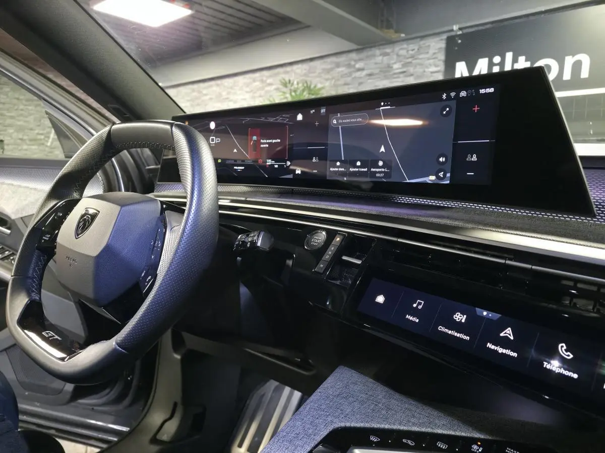 Vue intérieure côté conducteur du Peugeot 5008 gris 2025, avec volant compact GT et écran panoramique incurvé.
