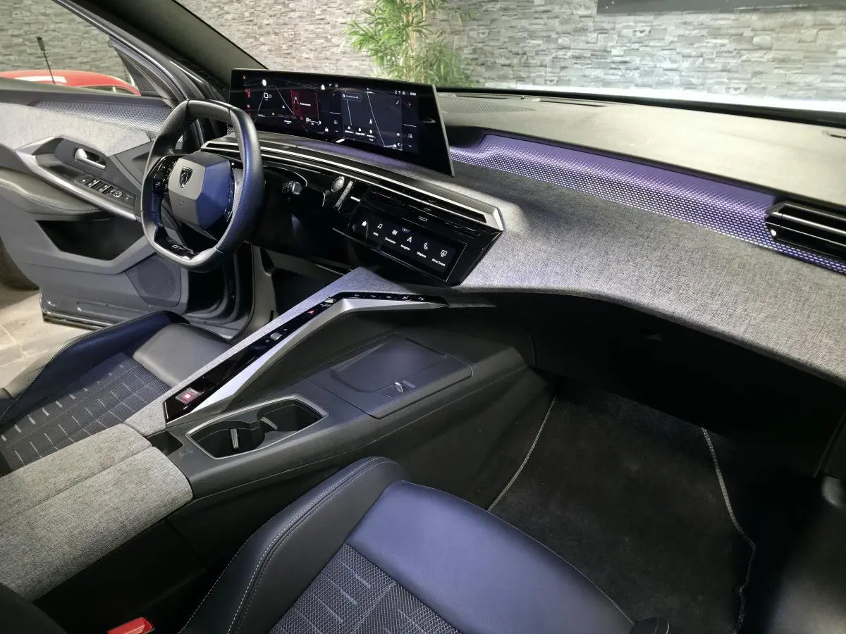 Vue intérieure côté conducteur du Peugeot 5008 gris 2025, avec planche de bord tissu Rimini et éclairage d'ambiance violet.