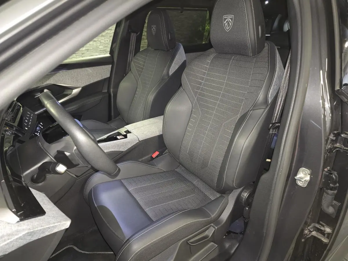 Vue intérieure côté conducteur du Peugeot 5008 gris 2025, sièges tissu et cuir avec logo Peugeot brodé sur les appuie-têtes.