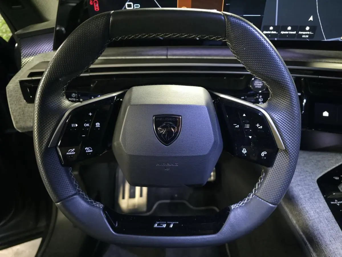 Vue rapprochée du volant noir perforé Peugeot 5008 GT avec commandes intégrées et logo central sur fond de tableau de bord numérique.