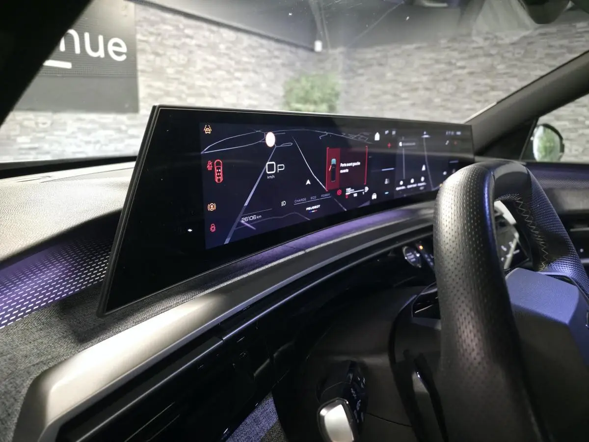 Vue intérieure du tableau de bord du Peugeot 5008 gris 2025, avec écran numérique panoramique et volant perforé noir.
