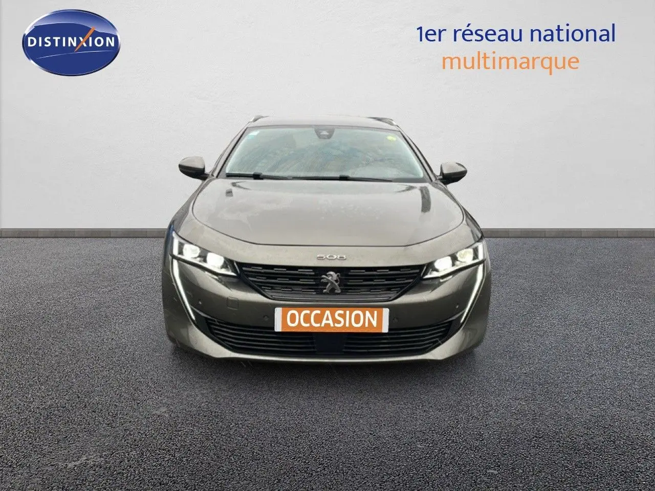 Vue frontale d'une Peugeot 508 SW gris amazonite métal avec phares allumés et plaque occasion.