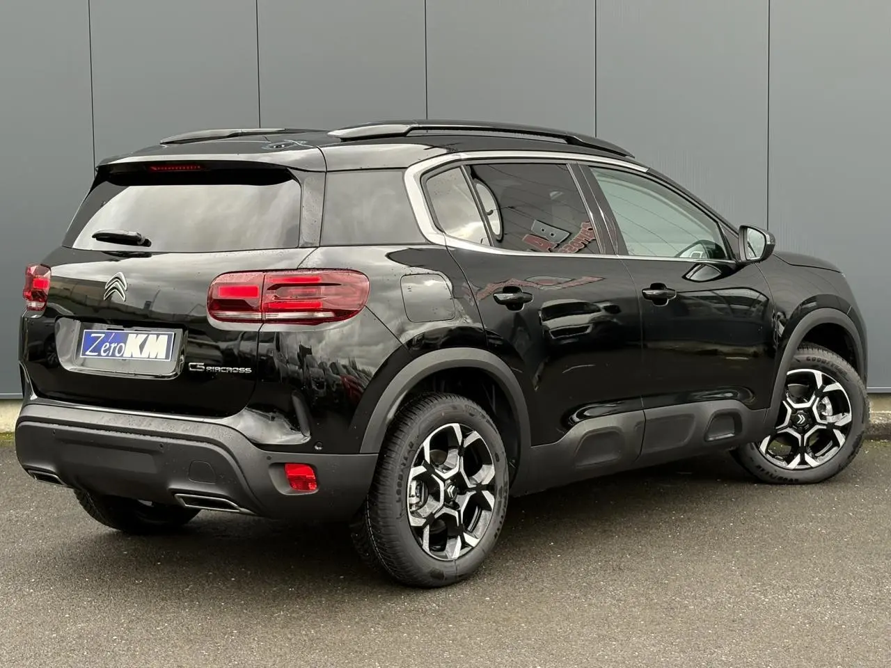 Vue 3/4 arrière droite d'un Citroën C5 Aircross noir Perla avec jantes alliage bi-ton et barres de toit noires.