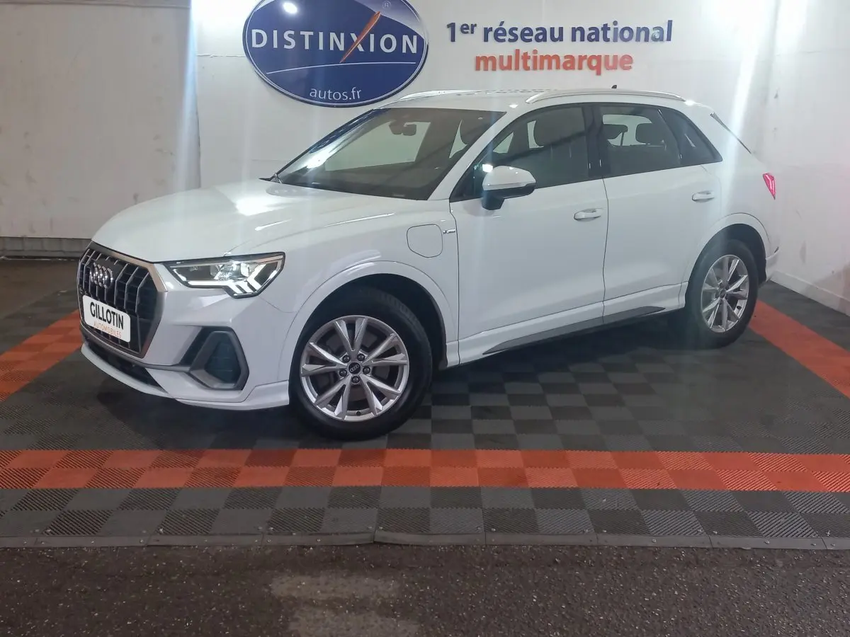 Audi Q3 blanc en vue de profil côté gauche, hybride rechargeable avec jantes alliage et calandre marquée S Line.
