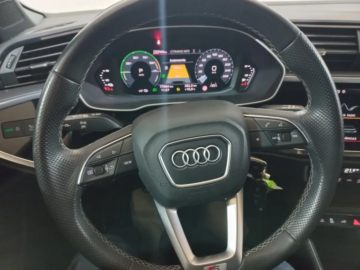 Vue rapprochée du volant cuir multifonctions et du tableau de bord numérique de l'Audi Q3 blanc hybride rechargeable.