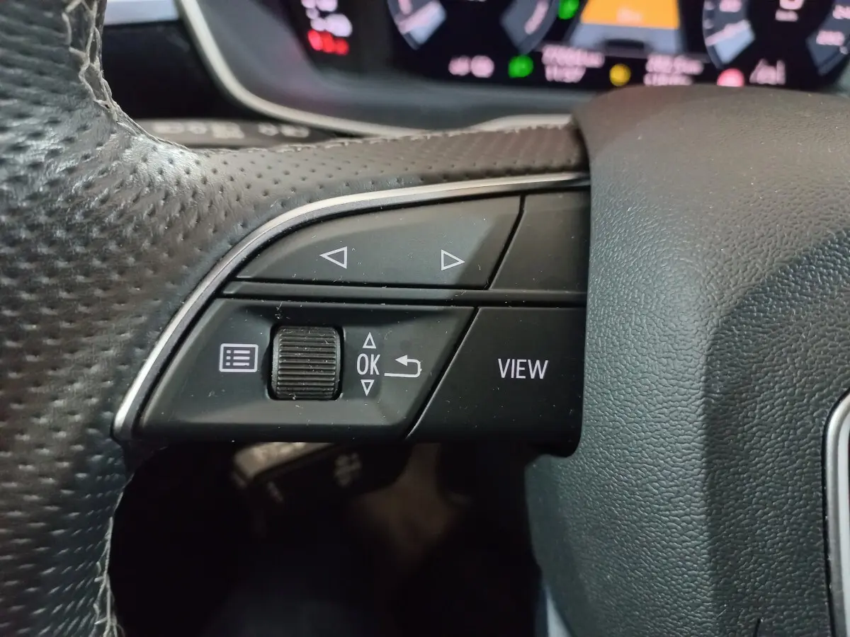 Gros plan sur les commandes gauche du volant cuir perforé de l'Audi Q3 blanc, version hybride rechargeable 2021.