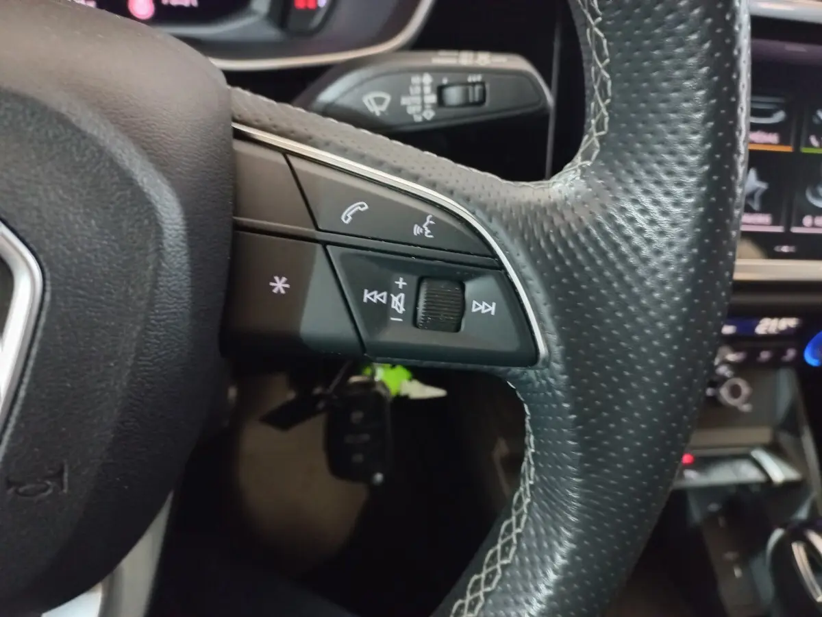 Gros plan sur la partie gauche du volant en cuir perforé de l'Audi Q3 blanc, avec commandes audio et téléphone intégrées.