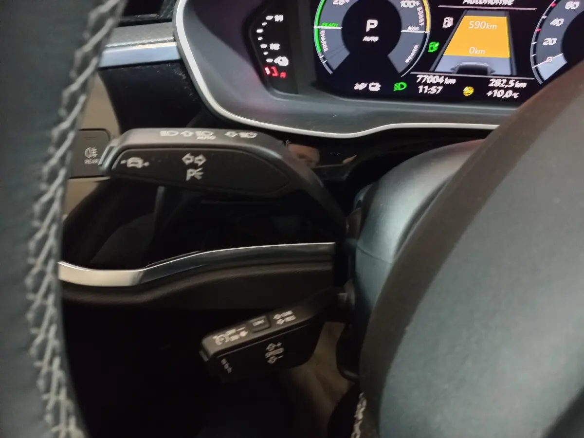 Gros plan sur le volant et les commandes de clignotants d’un Audi Q3 blanc hybride rechargeable, avec tableau de bord numérique visible.