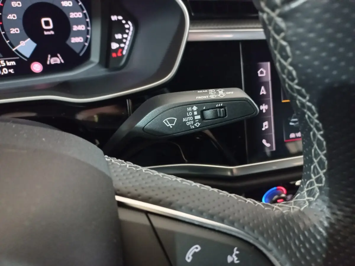 Gros plan sur la commande d’essuie-glace à gauche du volant cuir perforé dans l’Audi Q3 blanc hybride rechargeable 2021.