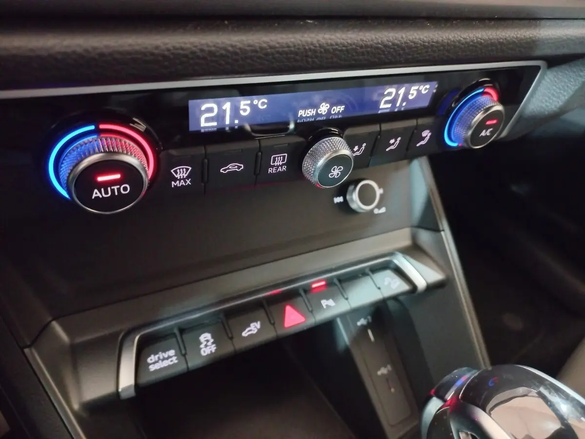 Gros plan sur la console centrale de l’Audi Q3 blanc, montrant les commandes de climatisation et les boutons multifonctions.
