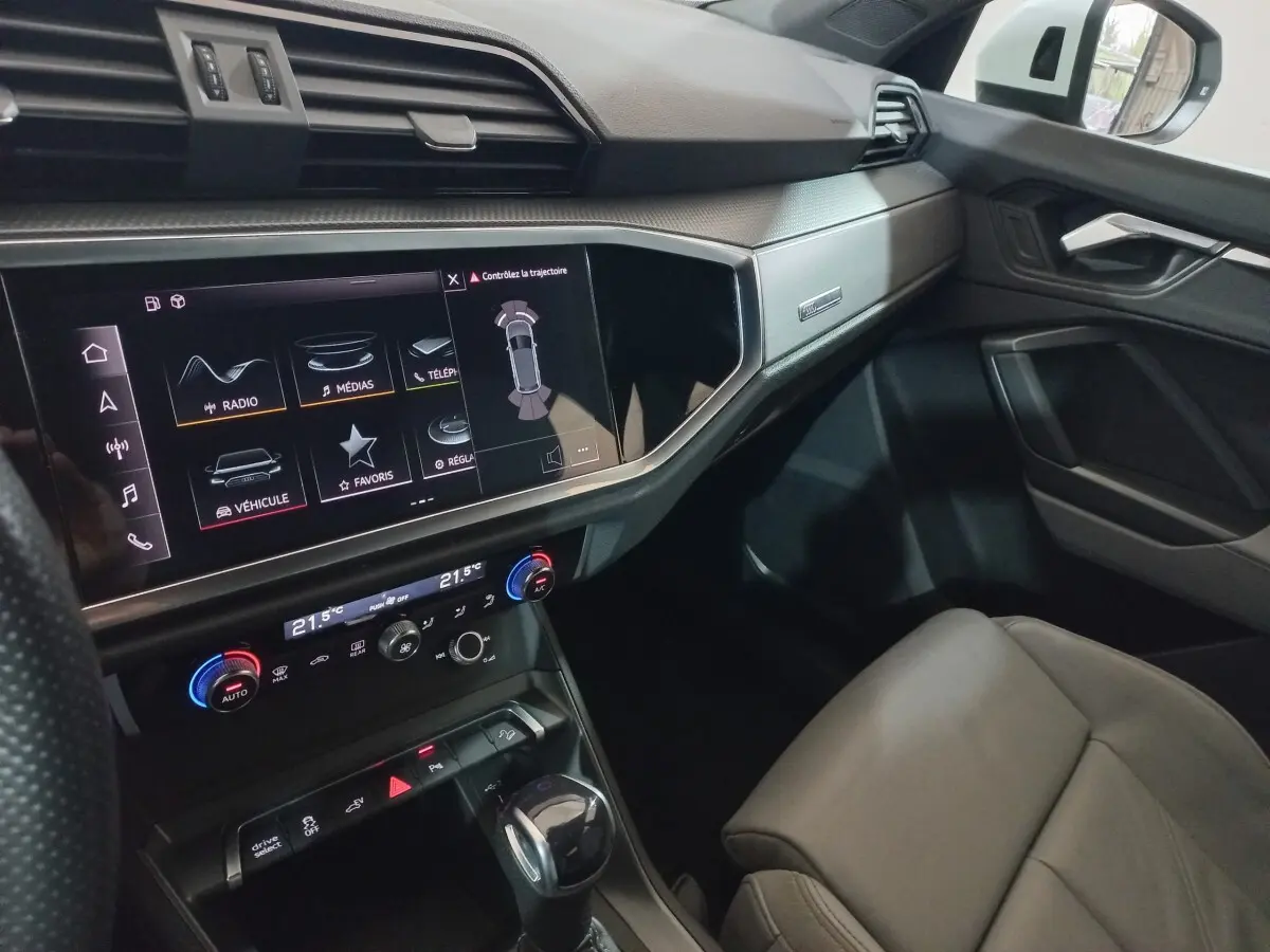 Vue intérieure côté passager de l'Audi Q3 blanc, mettant en valeur l'écran tactile central et la console moderne.