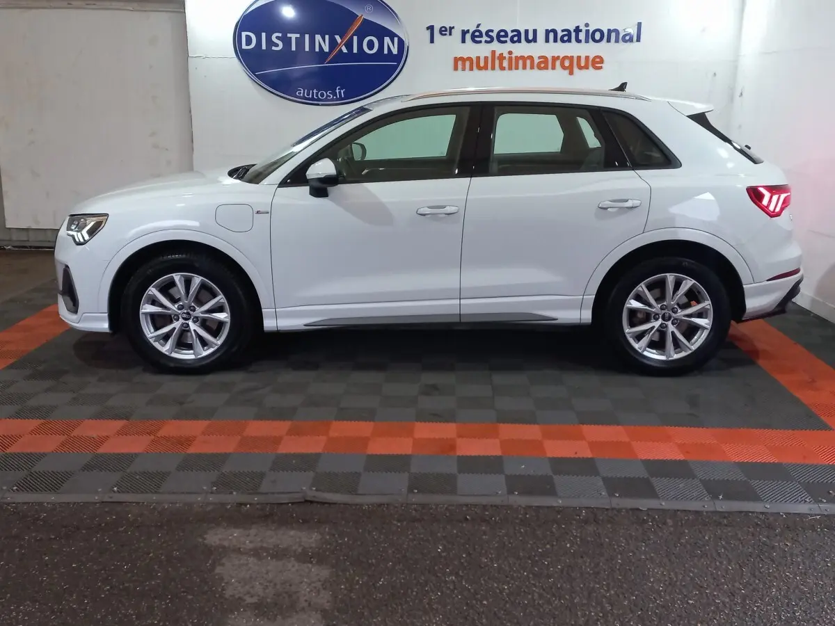 Profil droit d'un Audi Q3 blanc hybride rechargeable, avec jantes alliage et feux arrière LED allumés.