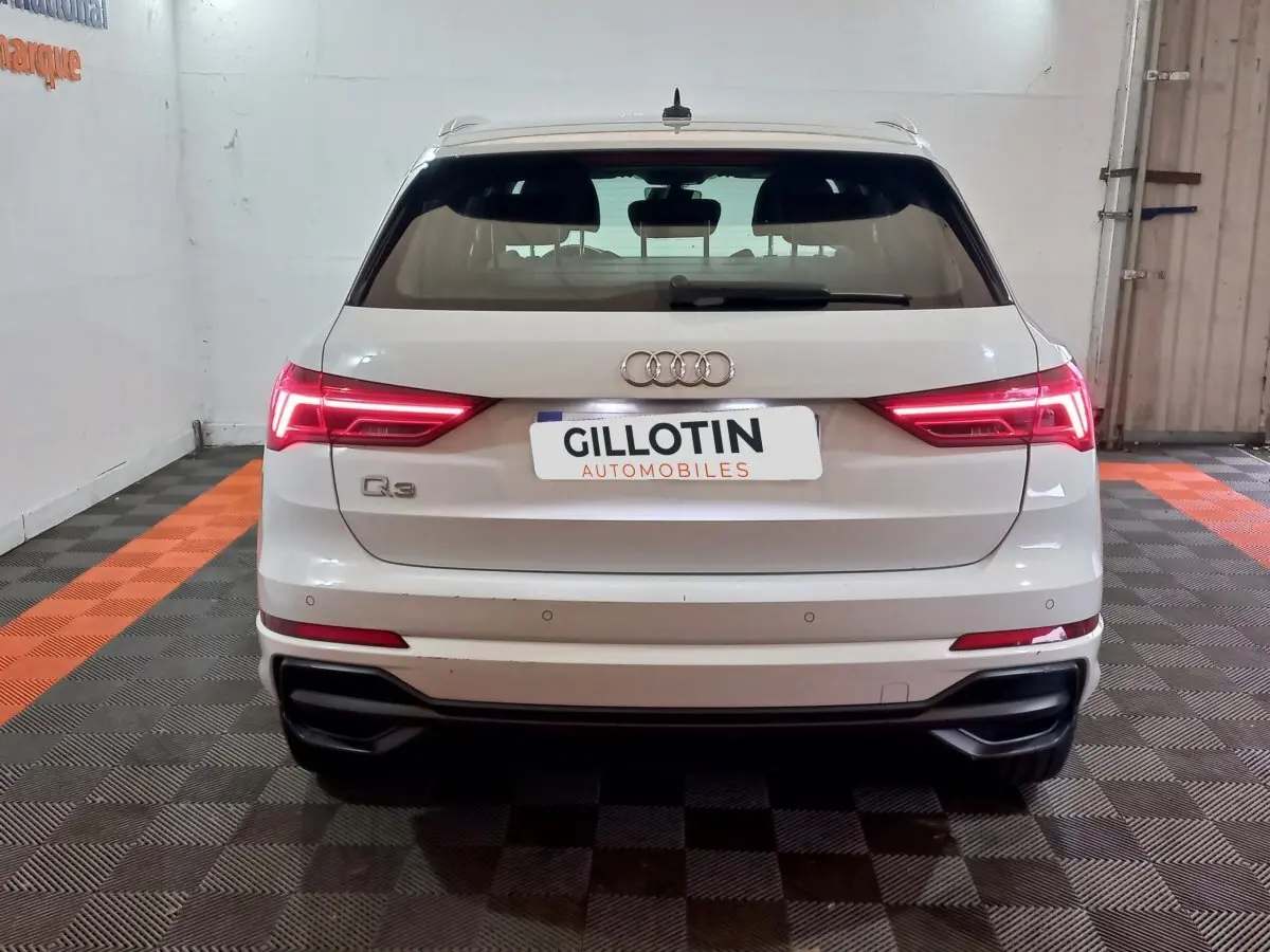 Vue arrière d’un Audi Q3 blanc 45 TFSI e 245 S tronic S line avec feux LED allumés en intérieur.