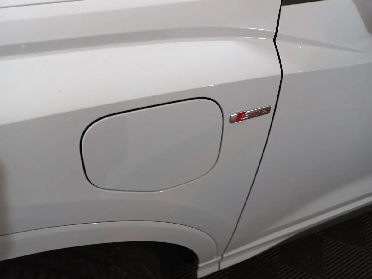 Gros plan sur la trappe de recharge côté gauche d’un Audi Q3 blanc avec badge S line visible.