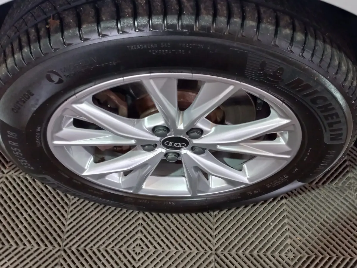 Gros plan sur la jante alliage argentée avec logo Audi au centre, montée sur pneu Michelin, véhicule blanc hybride Audi Q3.