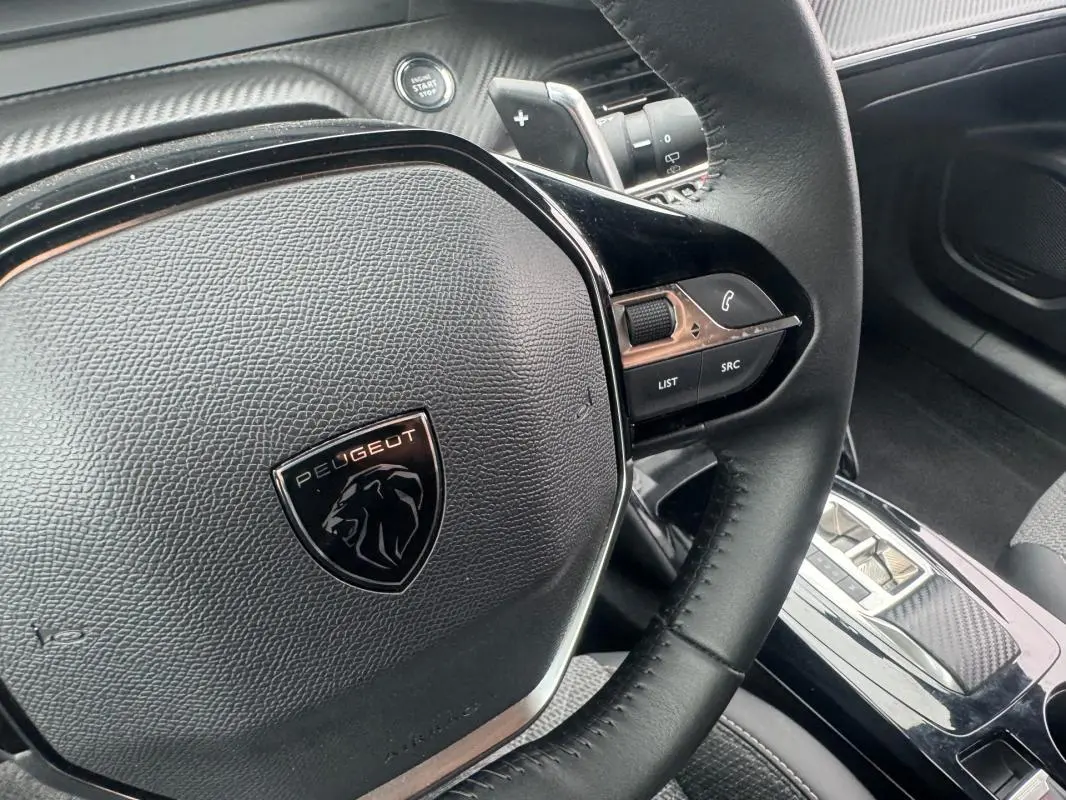 Gros plan sur le volant noir du Peugeot 2008 Hybrid 145 Allure, avec commandes intégrées et bouton start/stop visible.