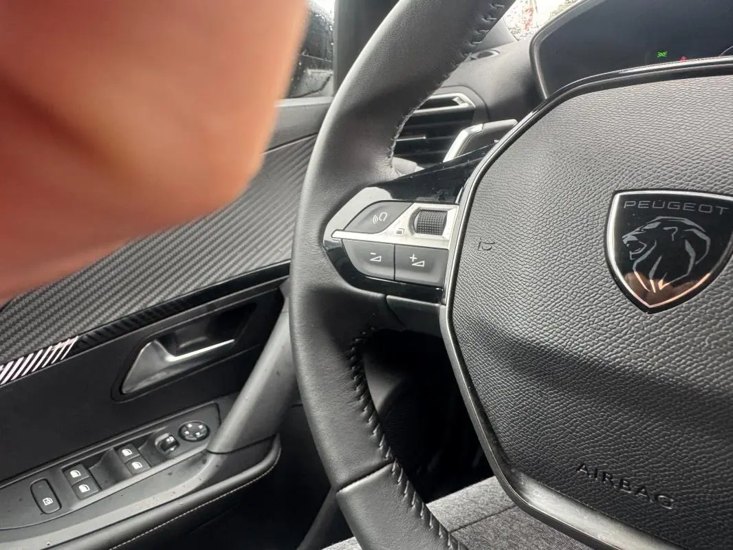 Gros plan sur le volant cuir noir du Peugeot 2008 Hybrid 145 Allure 2025 avec commandes intégrées et logo lion chromé.