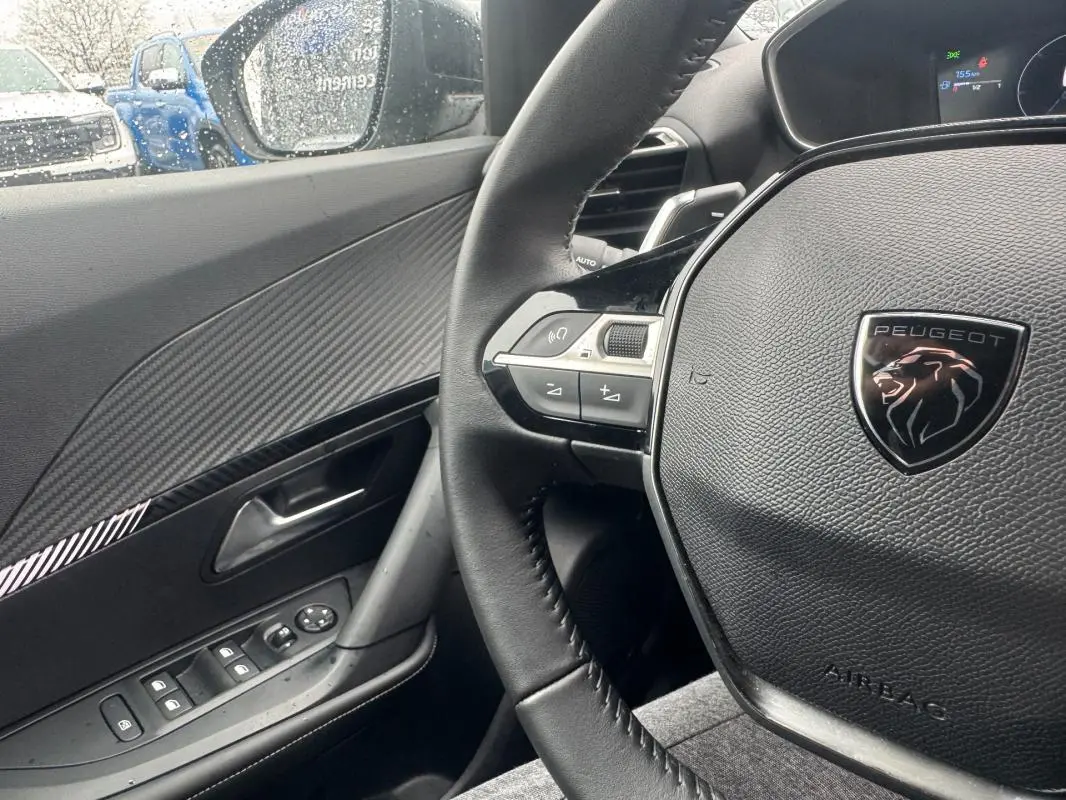 Vue intérieure côté conducteur du Peugeot 2008 gris 2025, volant cuir avec logo lion et commandes intégrées.