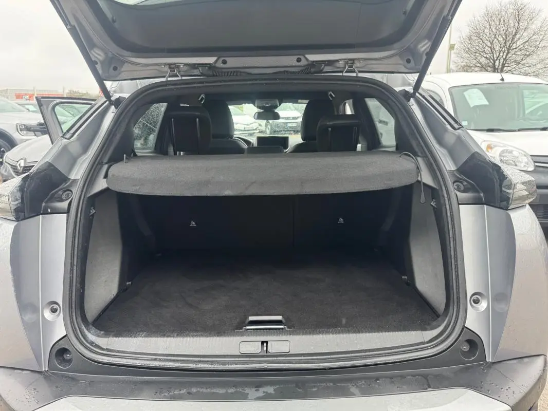 Coffre ouvert vu de l'arrière d'un Peugeot 2008 gris 2025, avec cache-bagages et intérieur sombre visible.