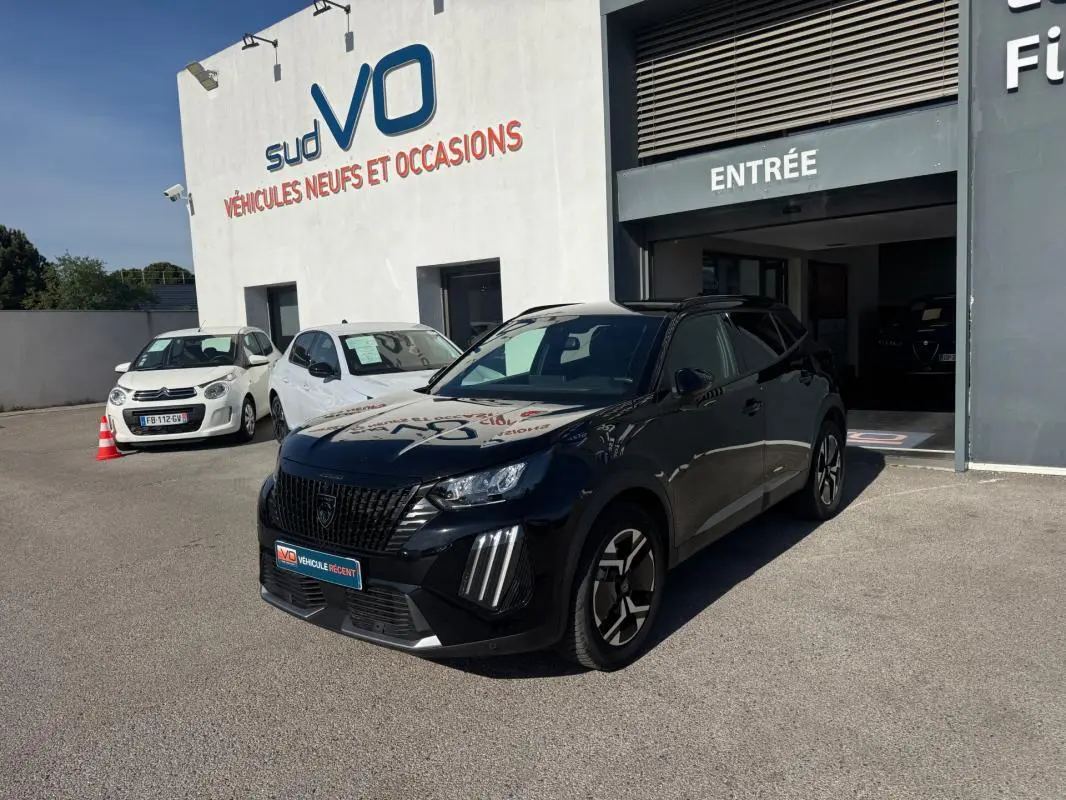 Peugeot 2008 Hybrid noir en 3/4 avant droit, avec barres de toit et jantes alliage 17 pouces, devant un garage.