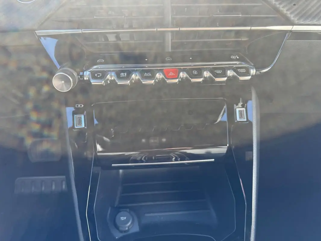 Vue rapprochée de la console centrale du Peugeot 2008 Hybrid 136 Allure 2025 noire, avec boutons de commande et prise 12V.