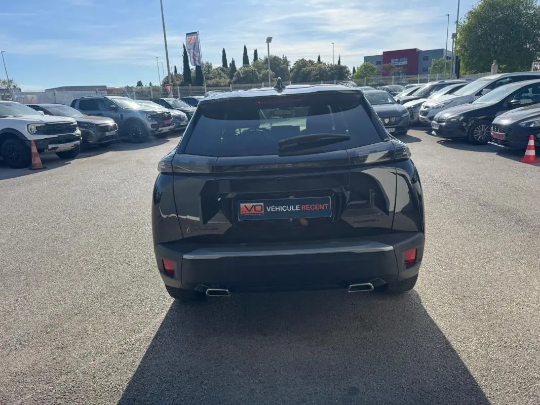 Vue arrière d'un Peugeot 2008 Hybrid noir 2025 avec barres de toit et jantes alliage 17 pouces, stationné en extérieur.