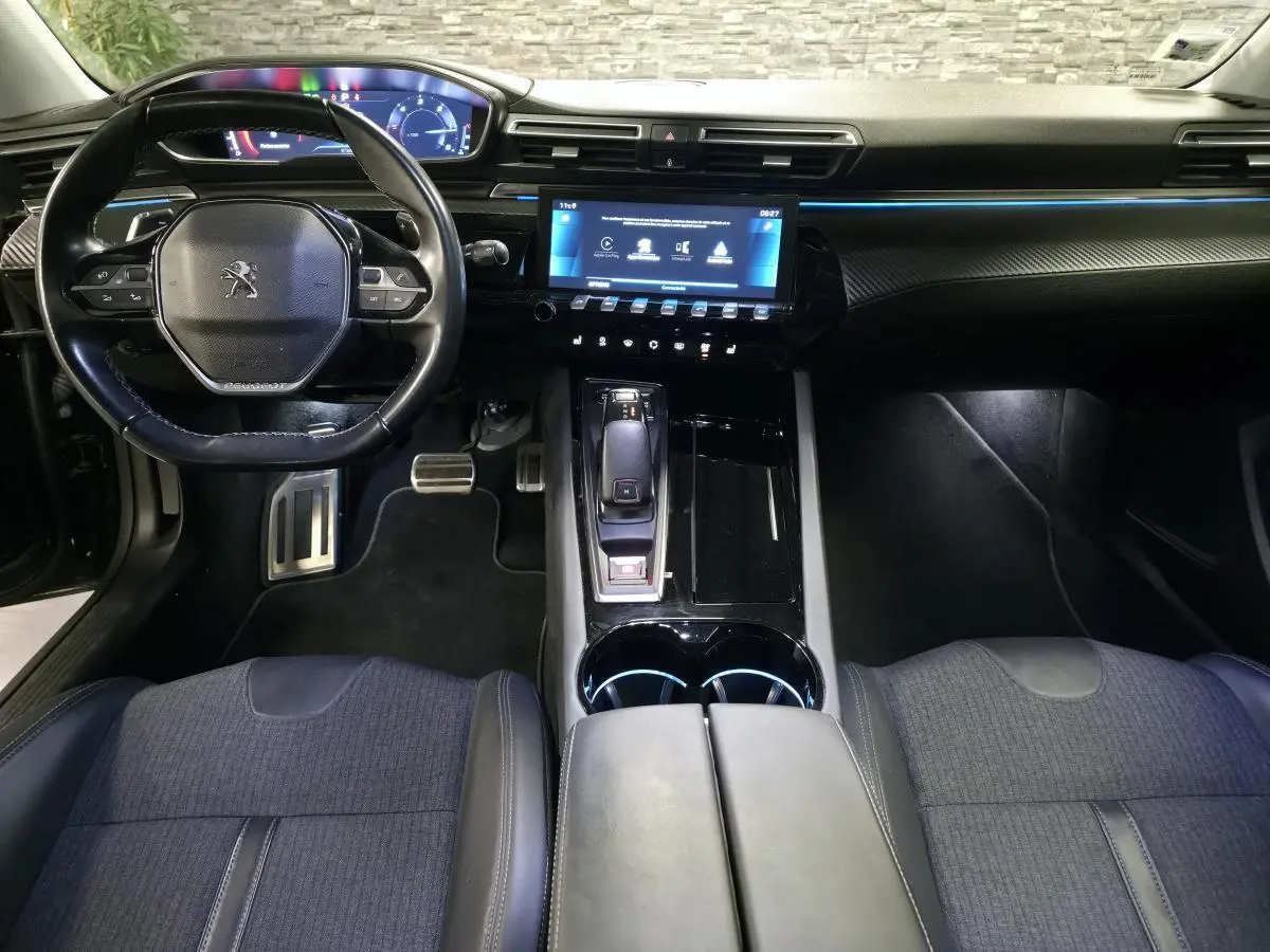 Vue intérieure avant de la Peugeot 508 SW noire, montrant le volant compact, l'écran tactile central et la console avec levier de vitesses.