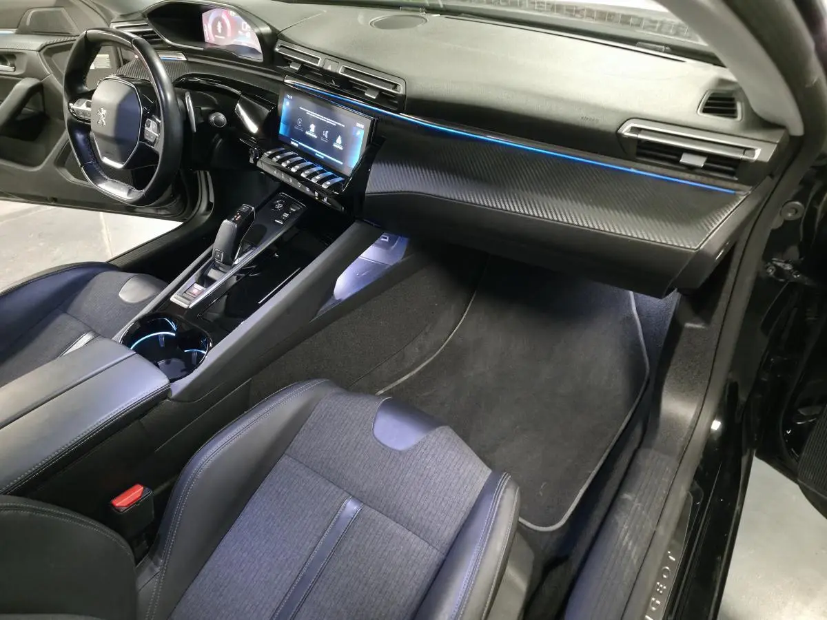 Vue intérieure côté passager de la Peugeot 508 SW noire, avec tableau de bord carbone et éclairage d'ambiance bleu.