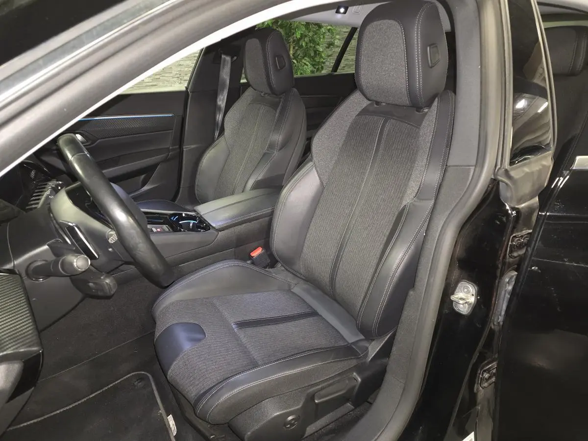 Vue intérieure côté conducteur de la Peugeot 508 SW noire, mettant en valeur les sièges tissu et cuir avec surpiqûres grises.