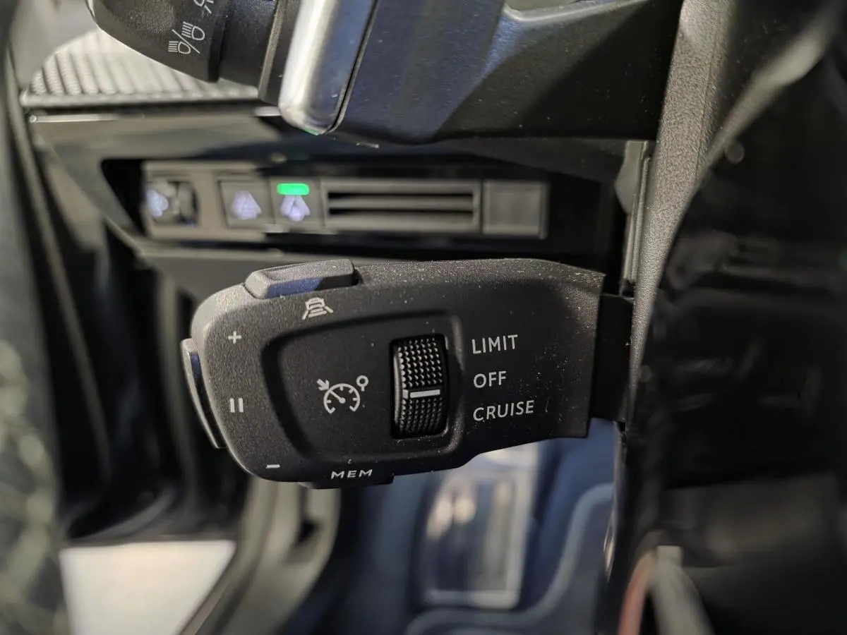 Gros plan sur la commande de régulateur de vitesse au volant d’une Peugeot 508 SW noire, intérieur sombre.