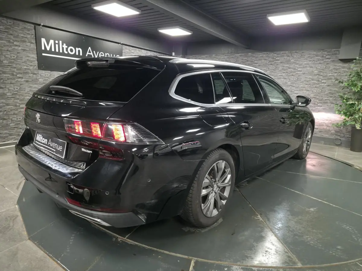 Peugeot 508 SW noire vue 3/4 arrière droit, avec feux arrière allumés et barres de toit aluminium.