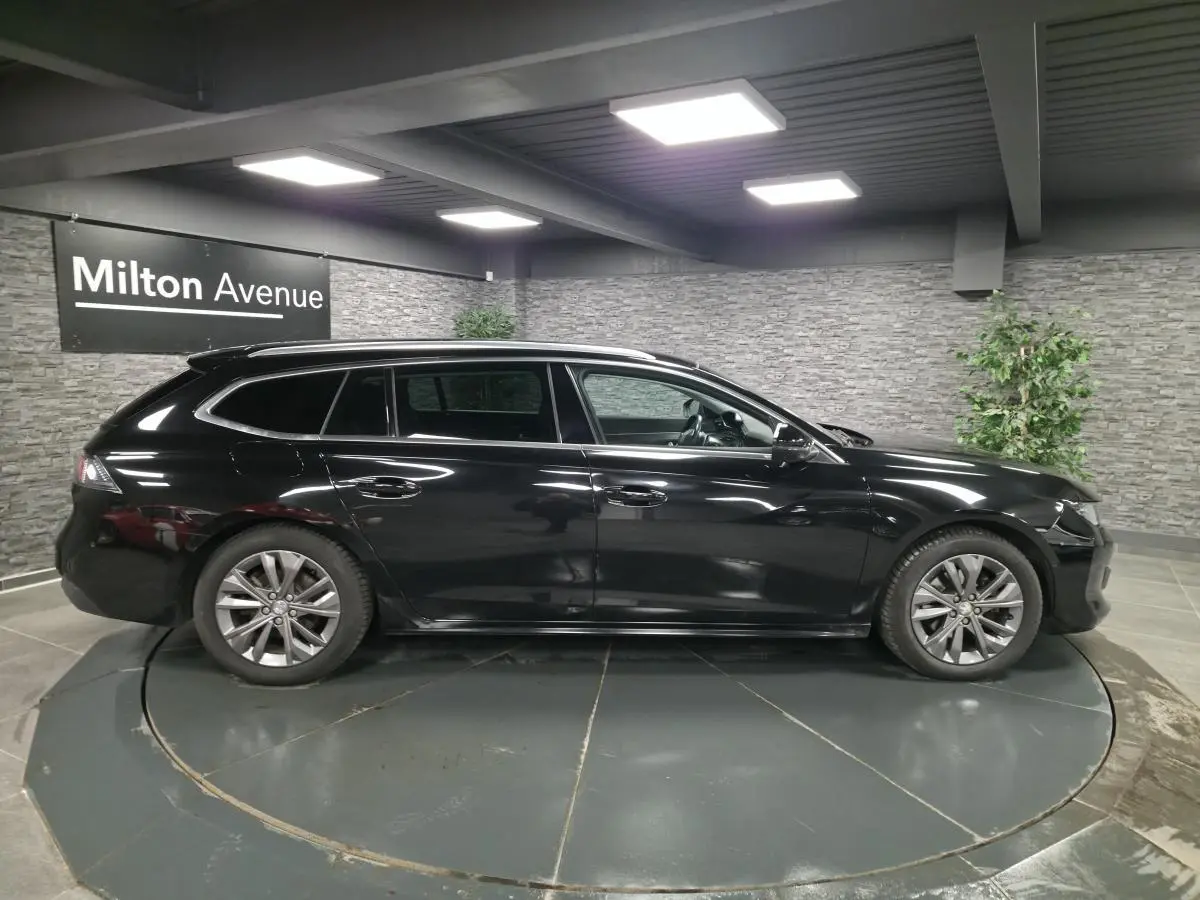 Profil droit d'une Peugeot 508 SW noire 2019 en stationnement intérieur avec barres de toit et jantes alliage 17 pouces.