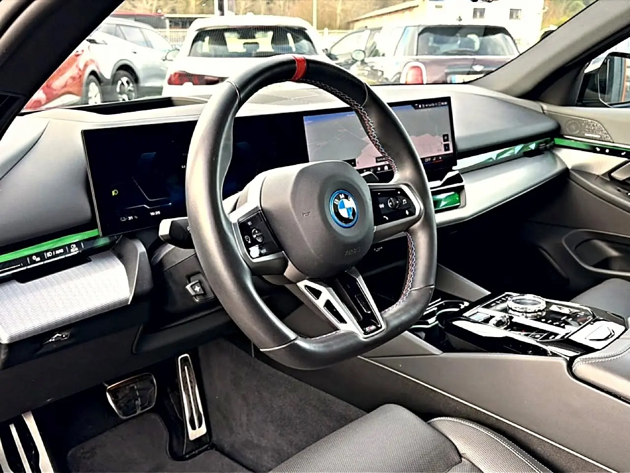 Vue intérieure côté conducteur de la BMW Série 5 i5 M60 2024 avec volant sport, écran tactile et inserts verts lumineux.