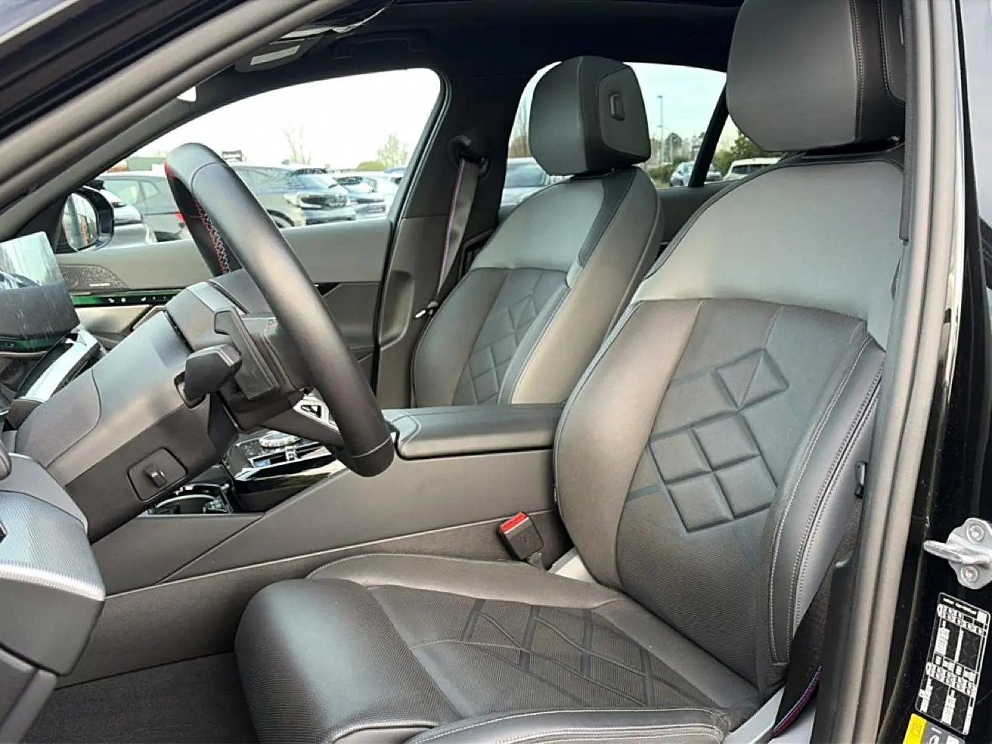 Vue intérieure côté conducteur de la BMW Série 5 i5 M60 2024 avec sièges en cuir noir et volant multifonction.