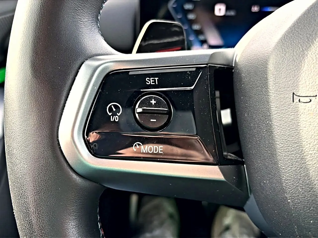 Gros plan sur les commandes de régulateur de vitesse à gauche du volant cuir noir d'une BMW Série 5 i5 M60 2024.