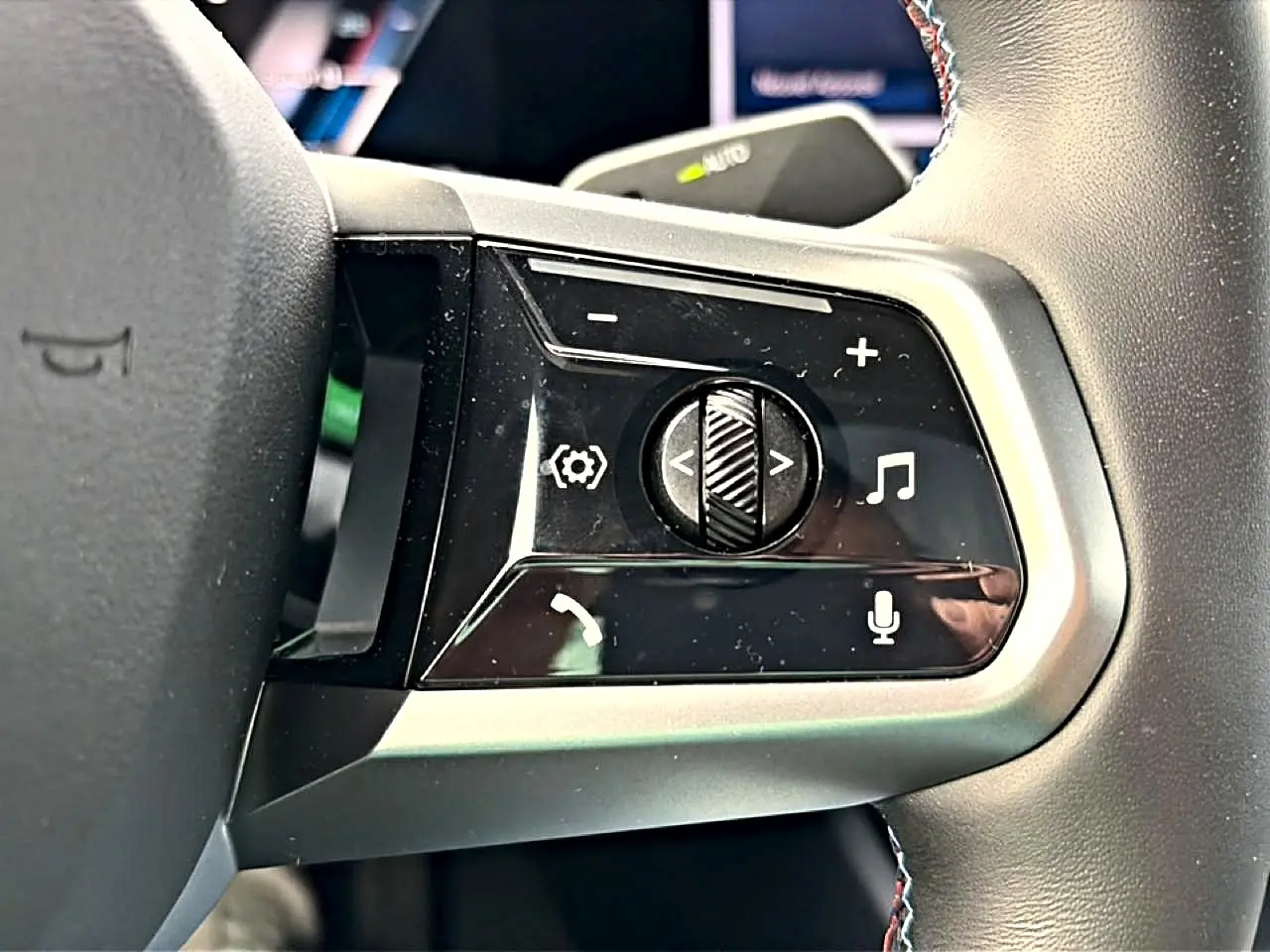 Gros plan sur les commandes multifonctions noires et argentées du volant cuir de la BMW Série 5 i5 M60 2024.